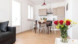 Una cocina moderna con armarios de madera, una mesa de comedor con sillas, un sofá de cuero negro y un jarrón con flores.