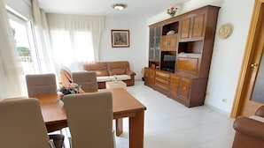 Una sala de estar con un sofá, una mesa de comedor con sillas, un mueble para televisor y un aparador.