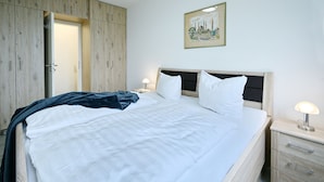 A neatly made bed with white linens, a wooden headboard, and a bedside lamp.