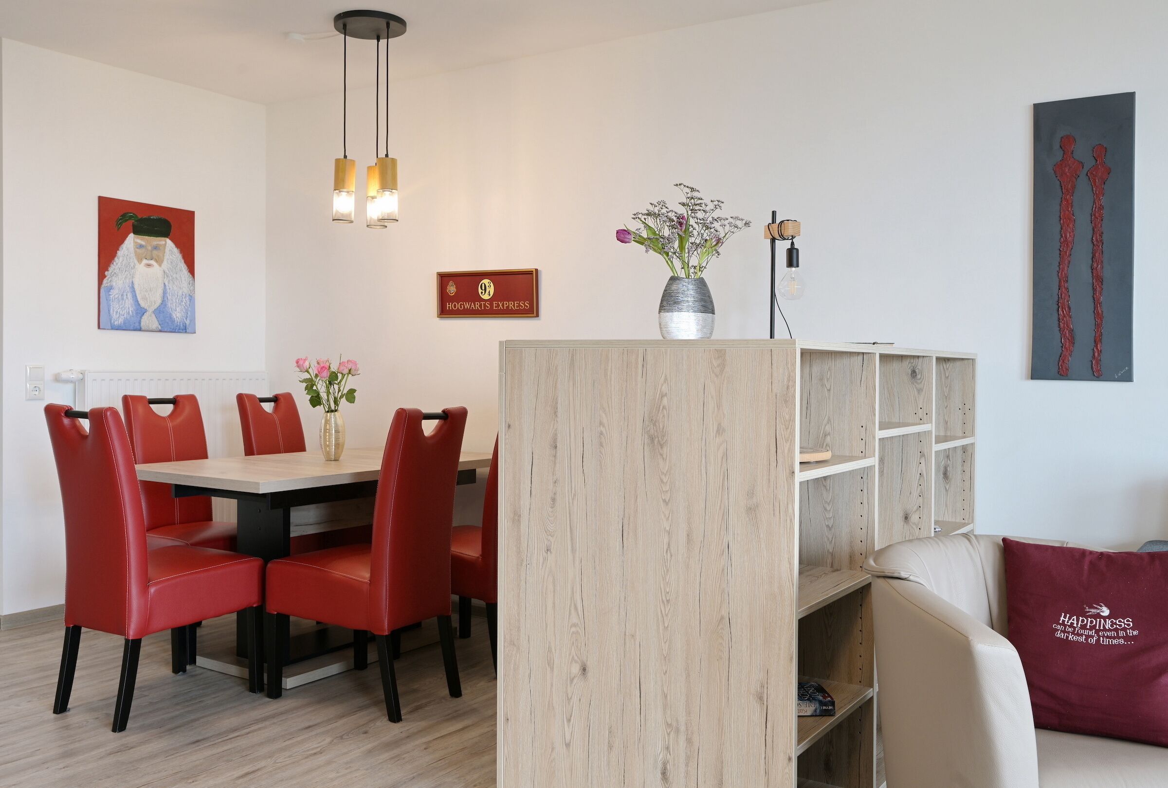 Un coin repas avec une table en bois et des chaises rouges, un vase rempli de fleurs et une pancarte sur laquelle on peut lire : « Poudlard Express ».