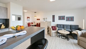 A modern living room with a grey sofa, a round coffee table, and a dining area with a wooden table and chairs.