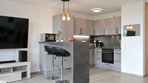 A modern kitchen with a built-in oven, a dining area with a bar stool, and a flat-screen TV mounted on the wall.