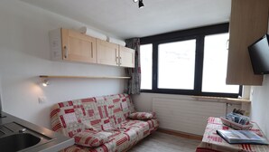 Une petite cuisine équipée avec un évier et une petite table, un canapé recouvert d’un tissu à motifs et une fenêtre avec des rideaux.