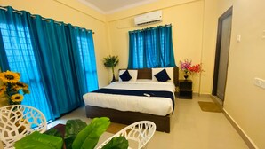 Una habitación de hotel con cama, cortinas, una planta en maceta y una silla.