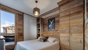 A bedroom with a bed, wooden walls, a ceiling light, a window, and a view of buildings outside. - Renovated apartment for 4, ski-in/ski-out, balcony, WIFI (Tignes)