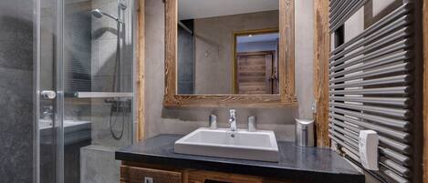 A modern bathroom with a glass shower enclosure, a wooden vanity with a sink, and a large mirror.