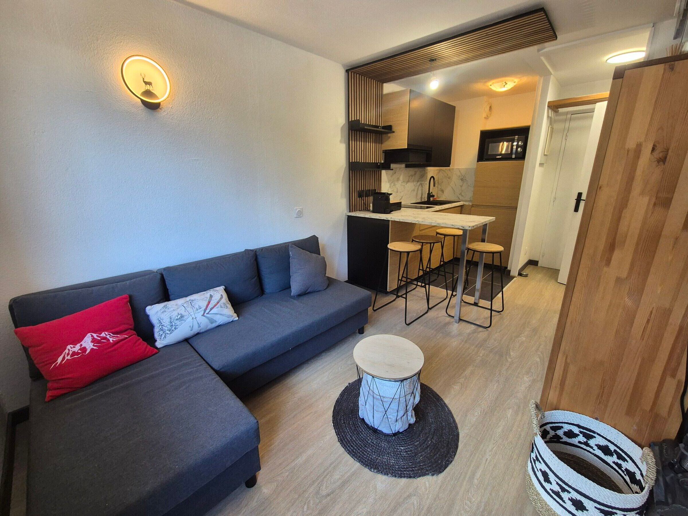 A modern living space with a sofa, a small round table, and a kitchen area with stools.