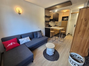 A modern living space with a sofa, a small round table, and a kitchen area with stools.