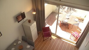 A balcony with a dining table, chairs, a refrigerator, and a chair with a striped cushion. - 6-person apartment with pool in Gruissan (Gruissan)