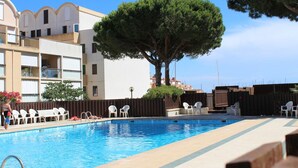 A swimming pool with a wooden deck, white chairs, and a large tree. - 6-person apartment with pool in Gruissan (Gruissan)