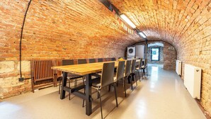 A spacious, brick-walled room with a long wooden table and chairs, a washing machine, and a radiator. - Welcome to your dream retreat at our exquisite loft-style villa. (Budapest)