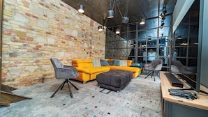 A modern living room with a brick wall, a yellow sectional sofa, a grey armchair, and a large window with multiple light fixtures. - Welcome to your dream retreat at our exquisite loft-style villa. (Budapest)