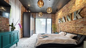 A modern bedroom with a brick wall, a large bed, a TV, and a 'BANK' sign. - Welcome to your dream retreat at our exquisite loft-style villa. (Budapest)