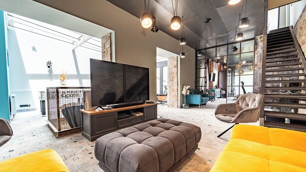 A modern living room with a large flat-screen TV, comfortable seating, and a staircase leading to an upper level. - Welcome to your dream retreat at our exquisite loft-style villa. (Budapest)