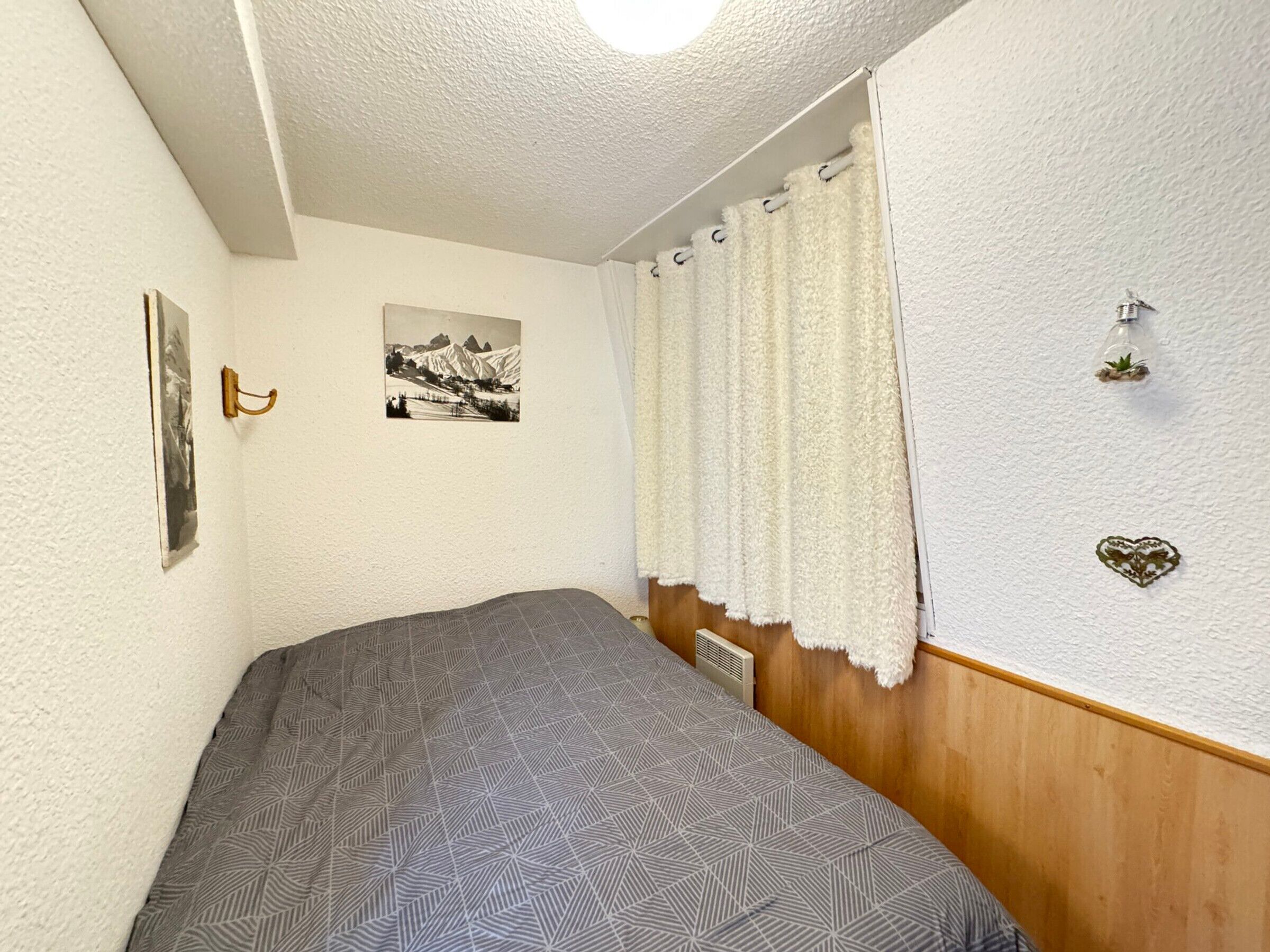 Un dormitorio con cama, un cuadro en la pared, una cortina y una planta pequeña.