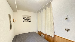 Un dormitorio con cama, un cuadro en la pared, una cortina y una planta pequeña.