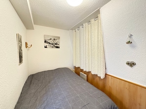 Une chambre à coucher avec un lit, un tableau accroché au mur, un rideau et une petite plante.