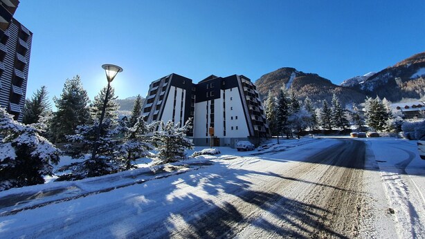 Un edificio moderno con techo plano, rodeado de árboles cubiertos de nieve y montañas al fondo.