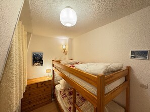 A bunk bed room with a wooden headboard, a bedside lamp, a small wooden dresser, and a ceiling light fixture.