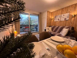 A dining area with a table set for two, a Christmas tree, and a view of a deck with outdoor furniture.