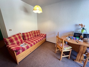 Et hyggeligt rum med en træsofa, et spisebord, en stol, en mikroovn og en hængende lampe.