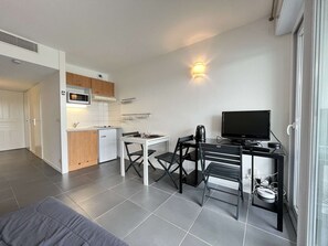 Quarto compacto com cozinha compacta, mesa de jantar com cadeiras, televisão e um banquinho pequeno.