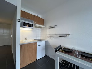 Cozinha compacta com micro-ondas, forno e pia. Há uma pequena mesa de jantar com cadeiras e uma cadeira com almofada preta.