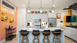 A modern kitchen with a central island, bar stools, and overhead lighting. - Hot Tub & Rooftop Views - Twang Town Terrace (Nashville)