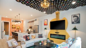 A modern living room with a large guitar-shaped fireplace, a dining area with a bar, and a kitchen in the background. - Hot Tub & Rooftop Views - Twang Town Terrace (Nashville)