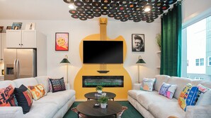 A living room with a large guitar-shaped TV, two sofas with colorful cushions, a small table with a plant, and a ceiling with vinyl records. - Hot Tub & Rooftop Views - Twang Town Terrace (Nashville)