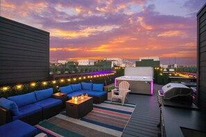 Un patio en la azotea con mesas al aire libre, una parrilla y luces colgantes.