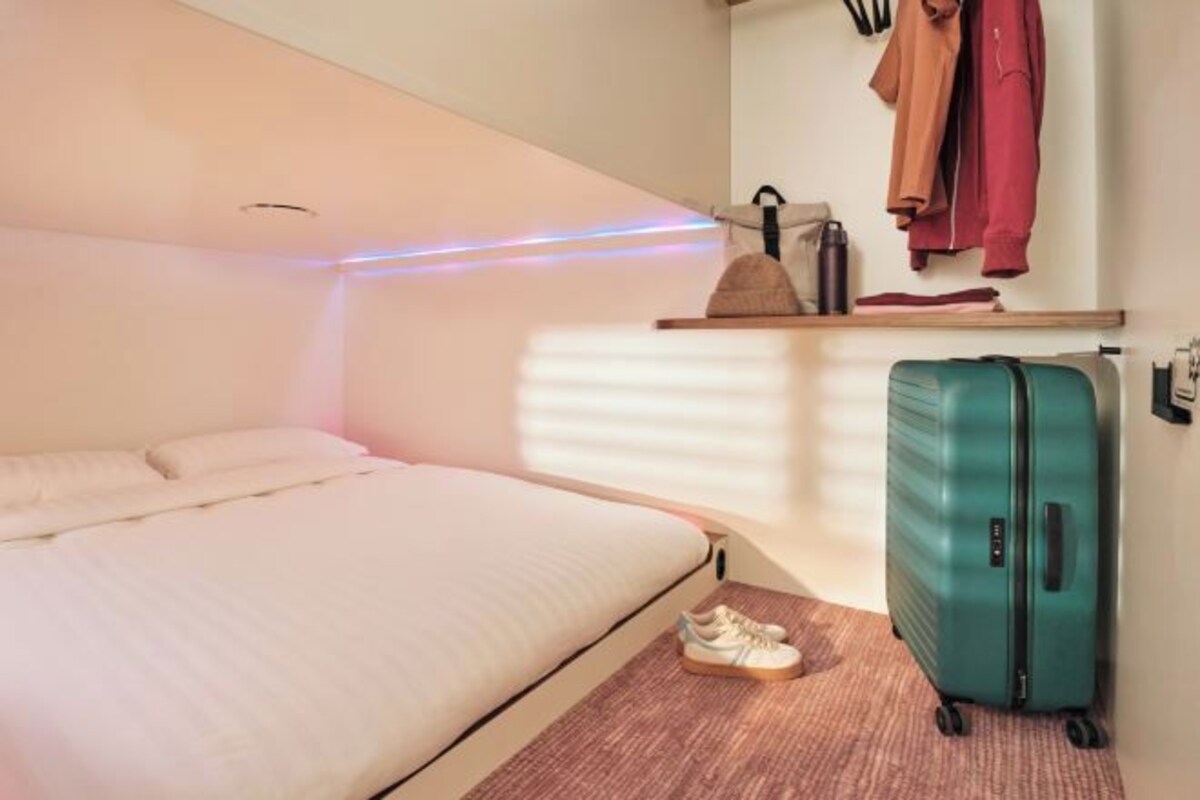 A bedroom with a bed, a suitcase, and a shelf with clothes and a bag.