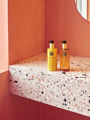 Deux flacons de lotion corporelle et de gel douche de la gamme Ritual of Meer, posés sur un comptoir en terrazzo.