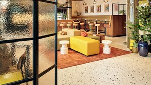 Un interior moderno con un sofá amarillo, mesas redondas blancas e iluminación colgante.