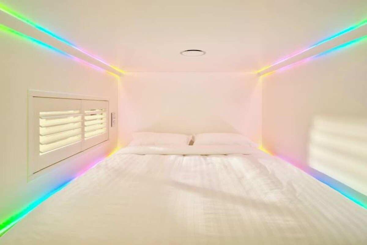 A bedroom with a bed, white walls, and a window with blinds.