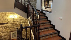 Una escalera con balaustres de madera, un muro de piedra y un ventanal con vitrales.