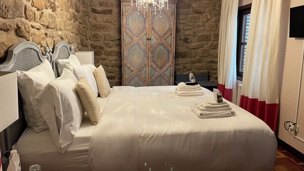 Una cama bien hecha con sábanas blancas, un candelabro y una pared de piedra.