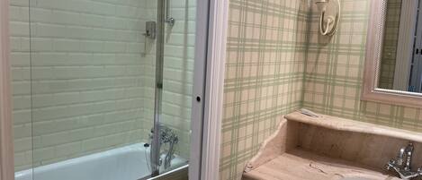 Un baño con ducha de vidrio, inodoro, lavabo con espejo y pared con estampado escocés.