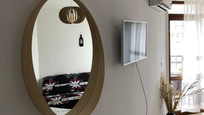 Et værelse med et stort rundt spejl, et fladskærms-tv på væggen, en potteplante og en sofa med et mønstret betræk.