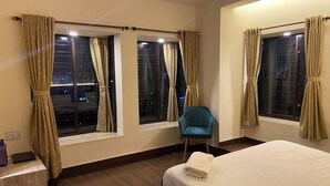 Una habitación de hotel con una cama, una silla y ventanas con cortinas.