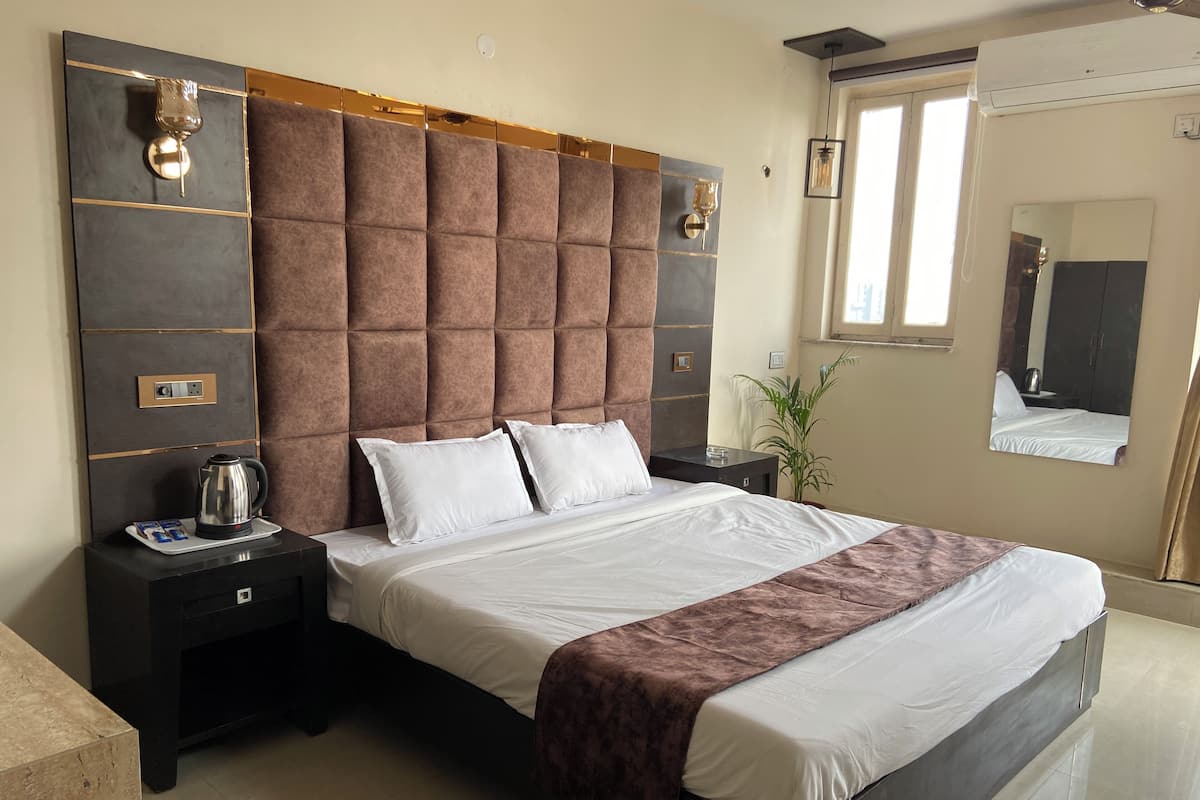 Quarto de hotel moderno com cama grande, mesa de cabeceira, cafeteira e espelho.