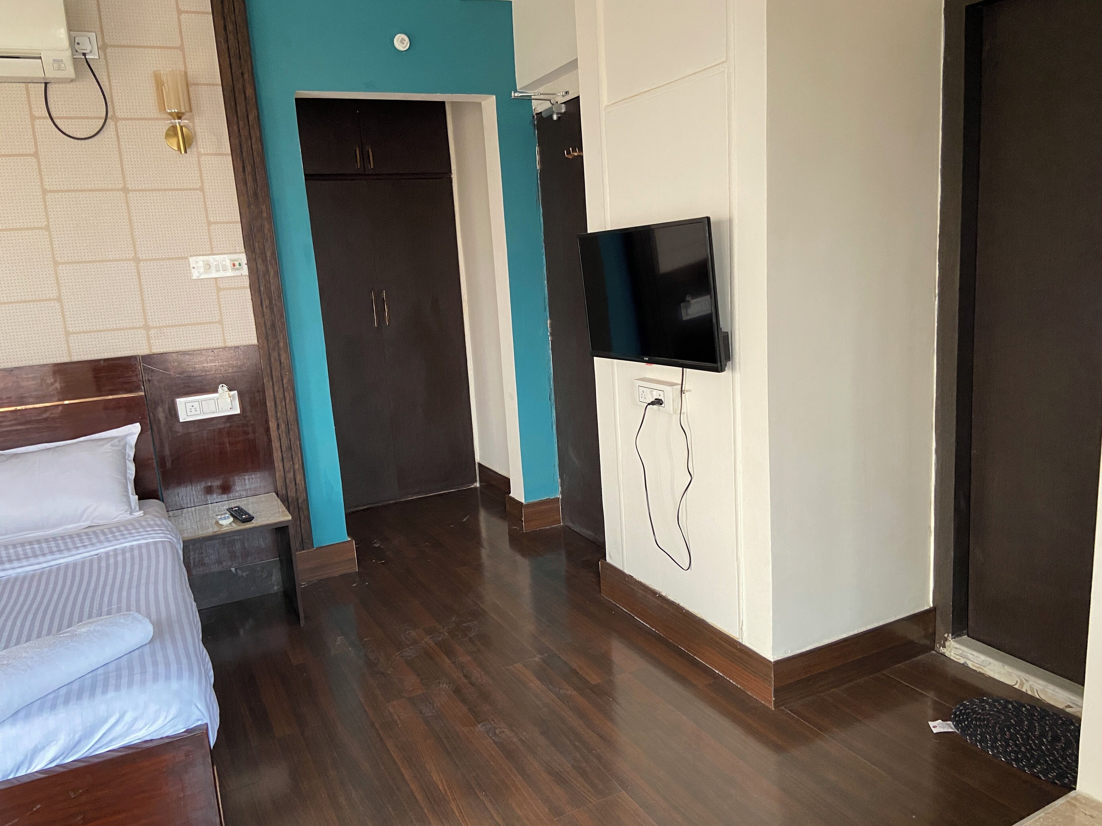 A hotel room with a bed, a TV mounted on the wall, a wardrobe, and a door leading to another room.