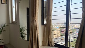 Una habitación con un ventanal grande, una planta en maceta y vistas a un paisaje urbano.