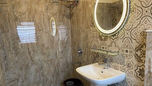 Un baño con pared de ducha de mármol, lavabo blanco y azulejos estampados.