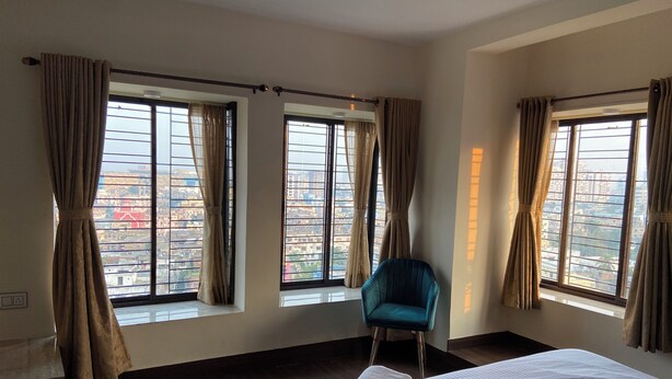 Una habitación de hotel con una cama grande, una silla azul y cortinas en tres ventanas.