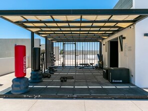 A covered outdoor gym area with exercise equipment, including a red punching bag and weightlifting stations.