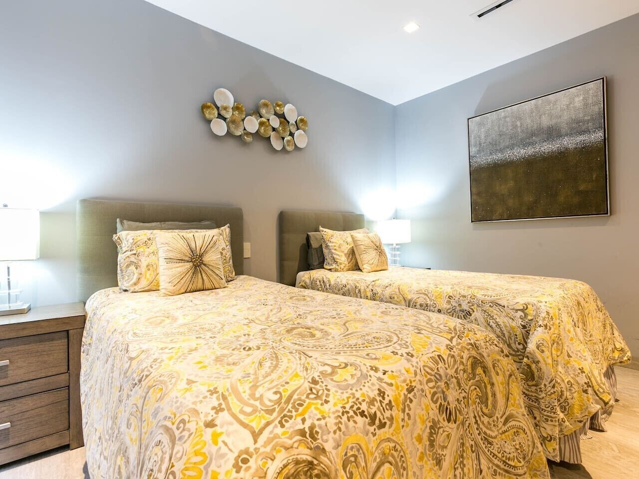 A bedroom with two beds, a bedside table, a wall-mounted artwork, and a decorative wall piece.