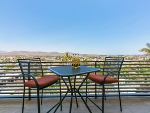 A balcony with two chairs and a table, overlooking a cityscape with mountains in the distance.