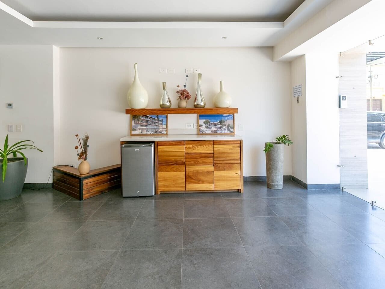 A reception area with a wooden cabinet, a small refrigerator, and a potted plant.