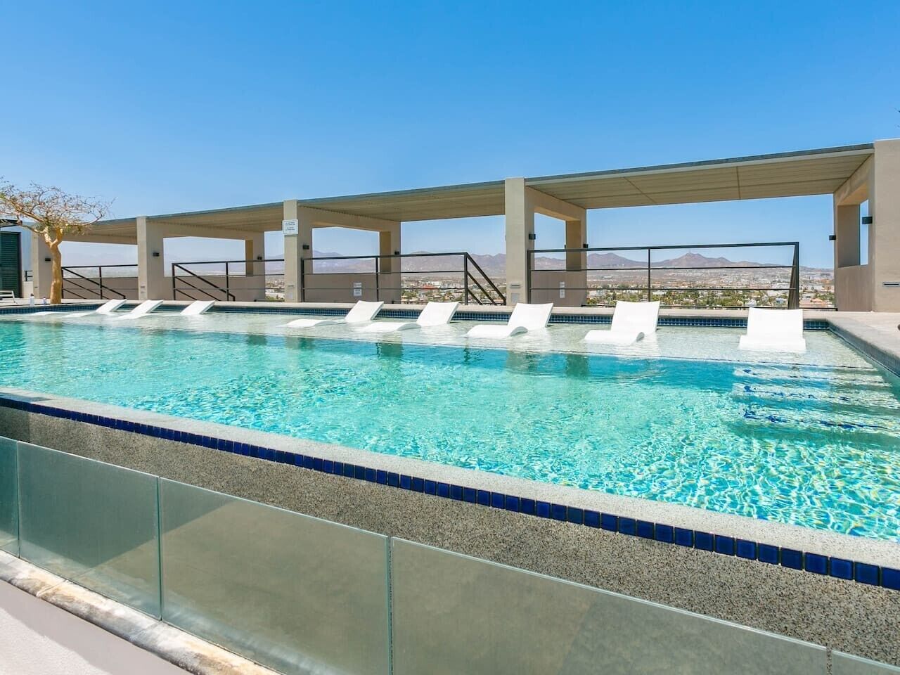 A swimming pool with clear blue water, surrounded by a covered area with white lounge chairs.